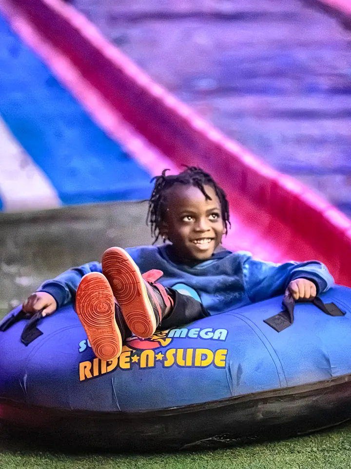 A kid grinning on a blue tube at the bottom of the holiday slide