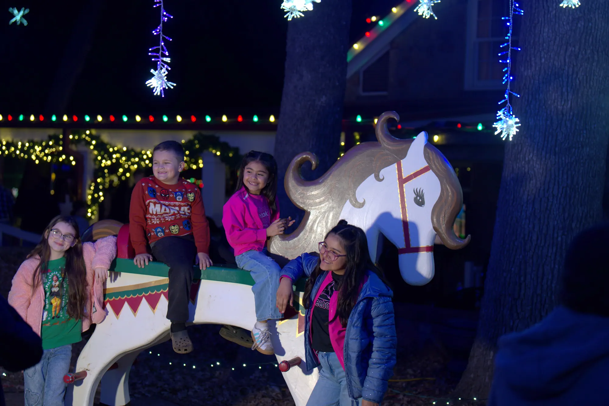Kids posing on a giant rocking horse under the lights